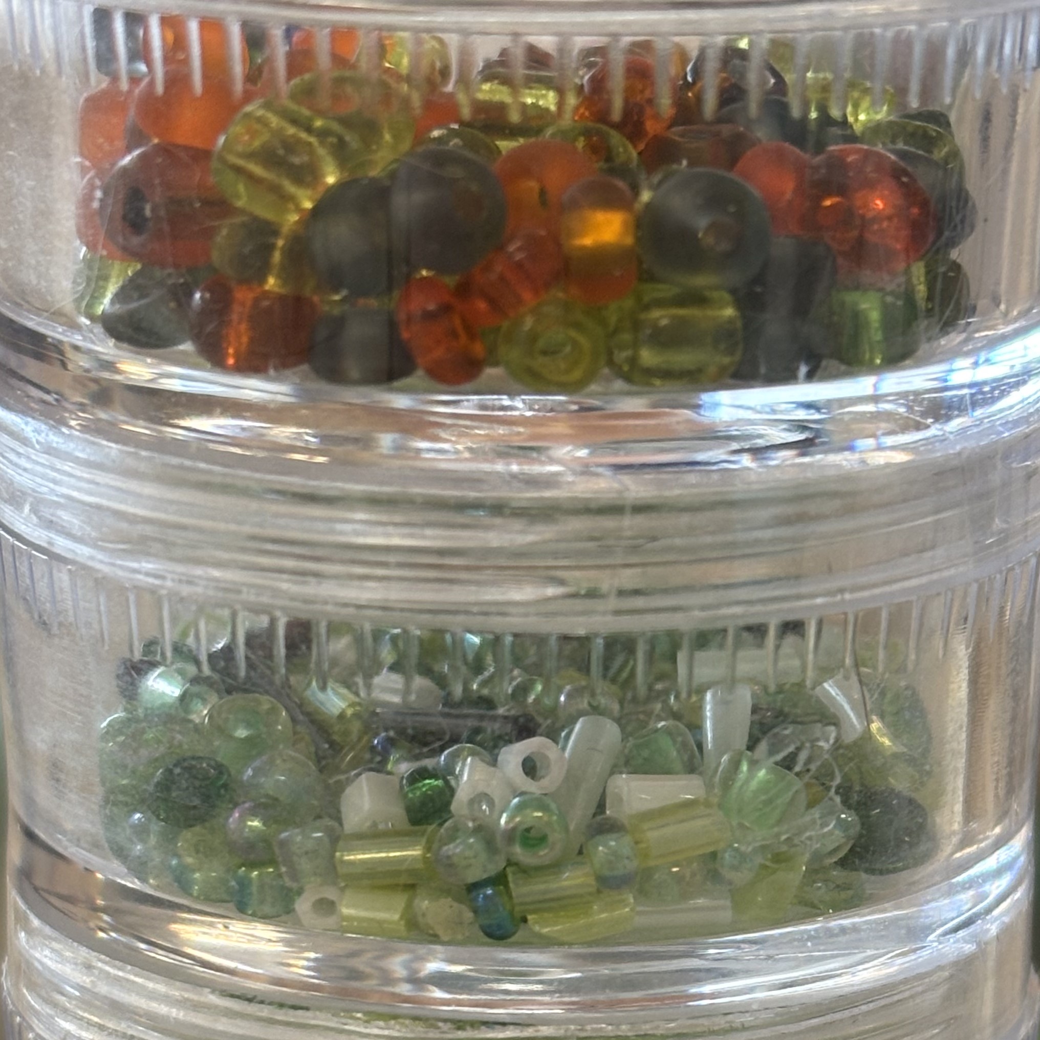 Small beads found in the textile department at Sheridan College. Made of plastic and used mainly for decoration. Regular shape with a smooth, reflective appearance. Some are transparent or semi-transparent.