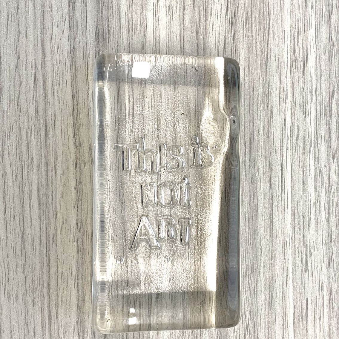 A glass block. The glass is transparent, smooth, and highly reflective. The glass refracts objects in a way that distorts the object behind the glass.